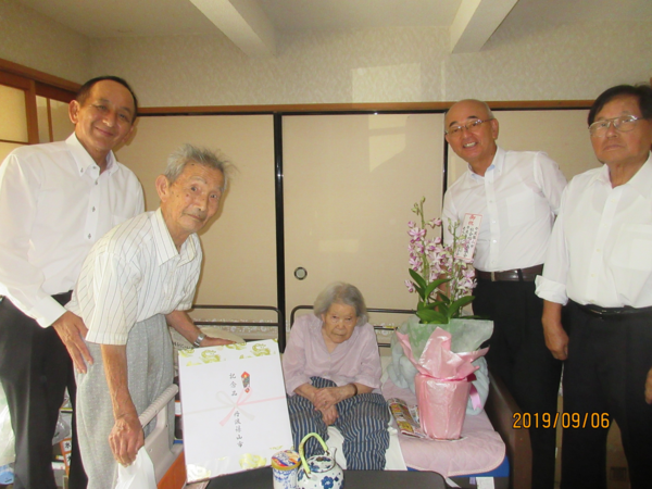 ベットで座っているご高齢の女性をお祝いしている写真