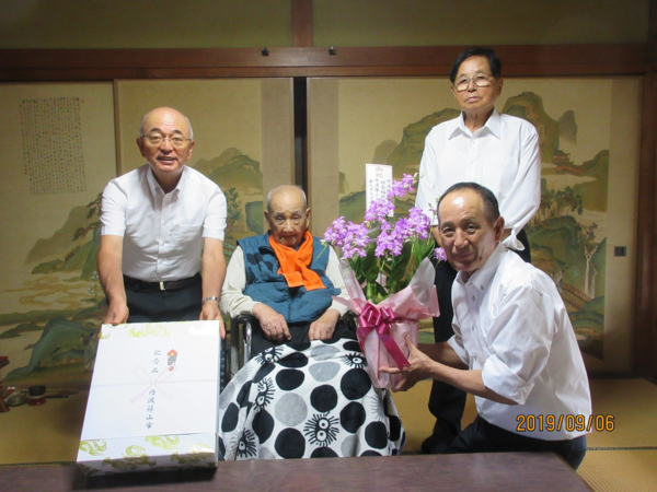 和室で車いすに座っているご高齢の男性の周りを3名が囲んでお祝いしている写真