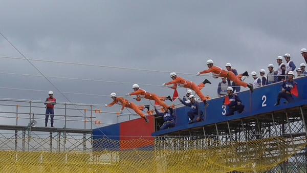 横向きに通されたロープの上を4名の消防隊員がロープの上にまたがり、腕の力で前に進もうとしている写真