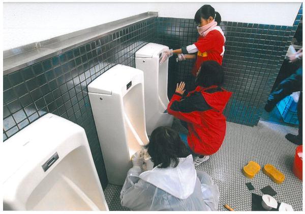 参加者の女の子と女性達が男子トイレの便器掃除をしている様子の写真