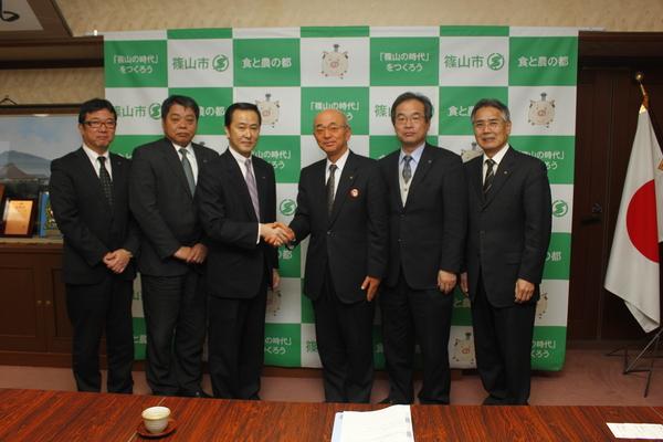 左側に近藤 雅彦社長、小林 喜美弘営業本部長、寺井 正海営業部部長、右側に酒井市長と市職員2名が立っており真ん中で近藤 雅彦社長と酒井市長が握手している写真