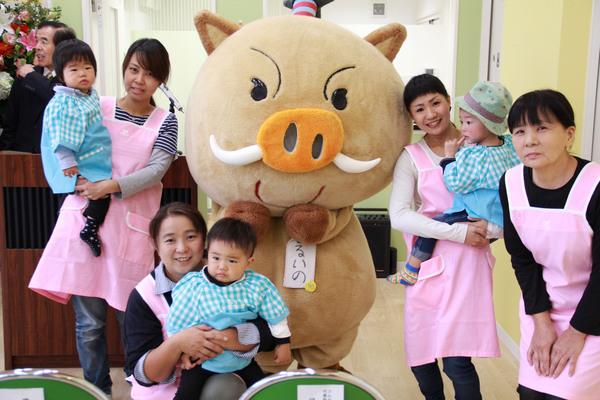 まるいのの横で、エプロンをつけた女性が子供を抱っこしている写真