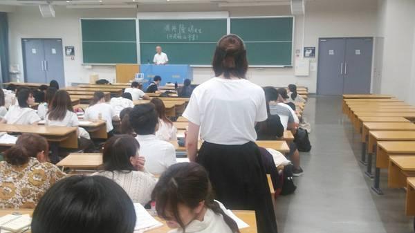 教室で、市長が壇上に立ち、生徒たちが座って聞いている中、女子生徒1名が立って発言している写真