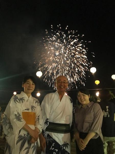花火が打ち上げられる中で市長が笑顔で女性2人と一緒に記念撮影写真
