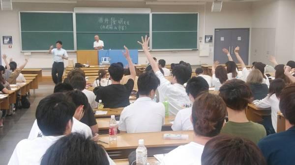 壇上で市長が腕組をしており、数名の生徒が手を挙げているのを男性が数えている写真