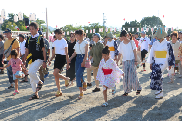 広場で大人も子供も片足を上げて踊っている写真