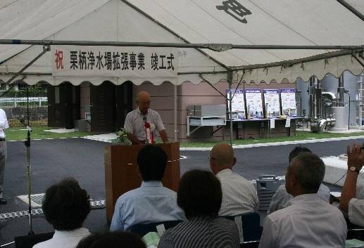 「祝 栗柄浄水場拡張事業 竣工式」と書かれた横断幕の前で、市長が話をしており、出席者が椅子に座って話を聞いている様子の写真