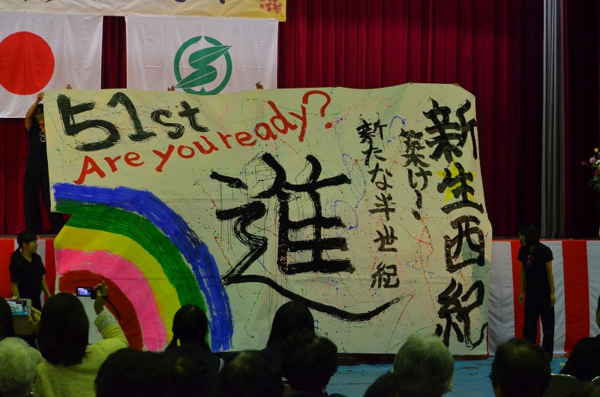 大きな布に進むという字が描かれていて、それを舞台で子供達が披露している写真