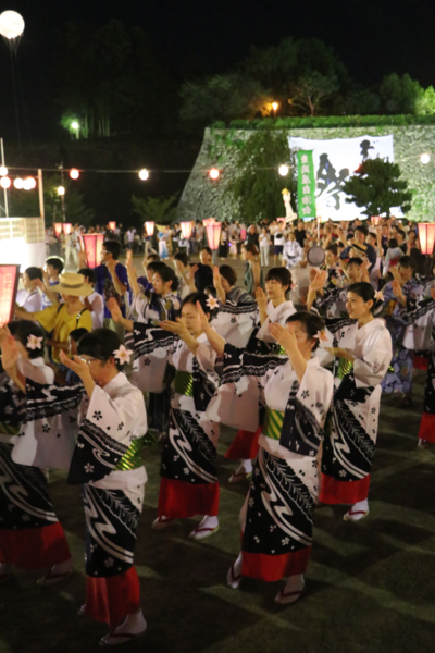 夜のお祭りで髪飾りをして浴衣に着替えた女性たちが手を広げて踊っている写真