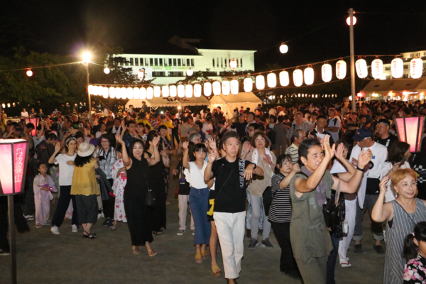 夜のお祭りで提灯がたくさんぶら下げられ周りで参加者が踊っている写真