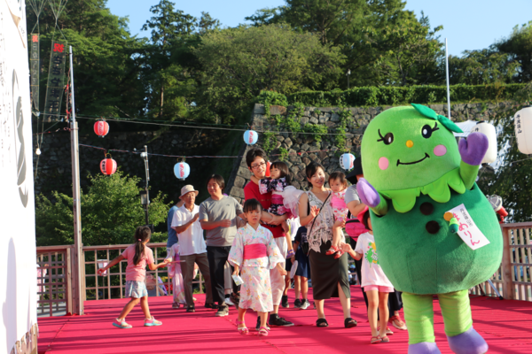 マスコット人形を先頭にその後ろから参加者が踊りながらついて行っている写真