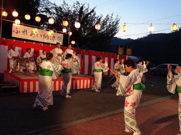 ステージで和楽器の演奏に合わせて歌う2名の女性と、その前で浴衣姿の女性らが盆踊りをしている写真