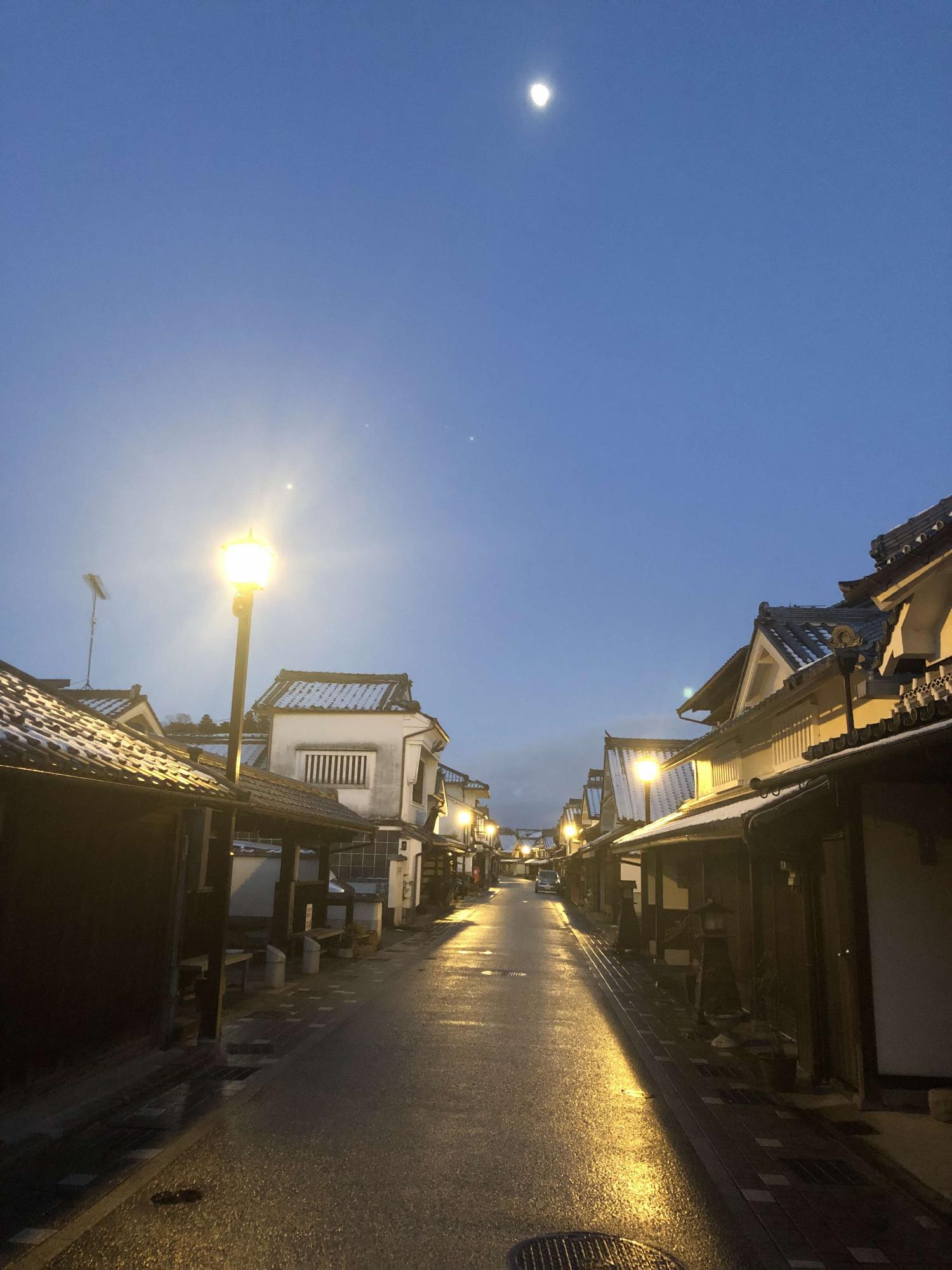 屋根にうっすら雪が残り、誰も歩いていない道路を街頭がぼんやり照らしている町並みの写真