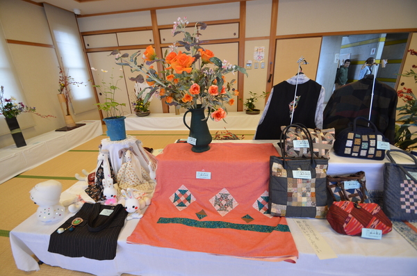 机の上に衣服や編み物作品が様々展示されている様子