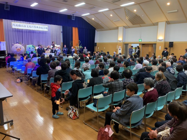 人々が椅子に座り舞台のまるいの、まめりんを観覧している様子の写真