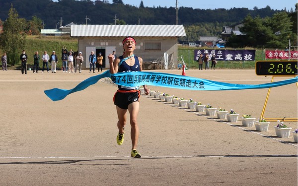 青いユニフォームを着た男子高校生がガッツポーズをしながらゴールテープをきっている瞬間の写真