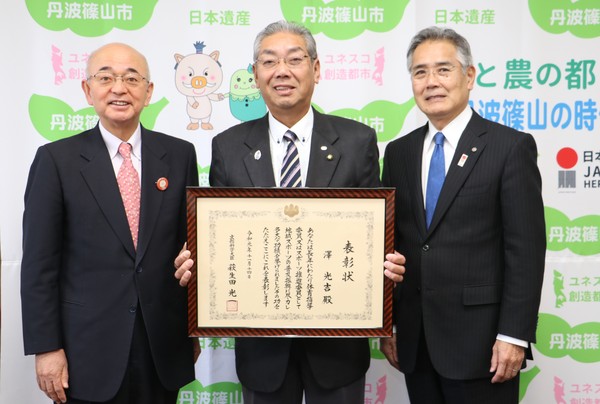 丹波篠山市と書かれた壁の前で、酒井市長、前川教育長、表彰状を持って笑顔の澤さんが並んでいる写真