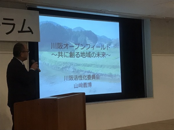 資料を投影したスクリーン横でマイクをもって話す山崎さん