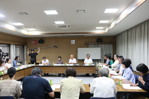 四角く輪にセットされた机いっぱいに座っている方々と中央で話をする市長、その様子を撮影するカメラマンや関係者