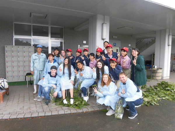 黒枝豆のさやを背景にワラワラ市から来られた方々が産業高校生とピースサインをしている様子