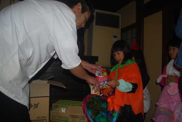 白い服をきた大人からお菓子をもらうハロウィーン衣装の女の子の写真