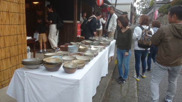 窯元店先に並べられた商品を見つめる女性客や通りを歩いている人々