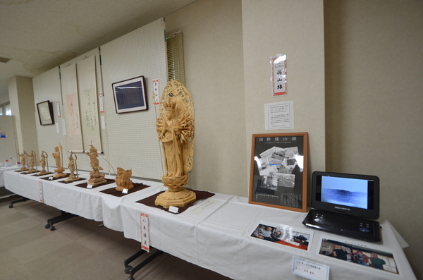 机の上に並べられた木彫り作品や映像を流し展示している様子