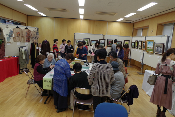 壁側に作品や写真が飾られ、中央の机を囲んで談笑する人々の写真