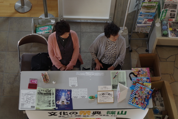資料や事務用品がおかれた机を前に二名の女性が椅子に座っている写真