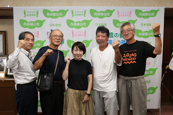 丹波篠山市と書かれた壁の前で仲田さんと福住地域の方々がガッツポーズをして立っている写真