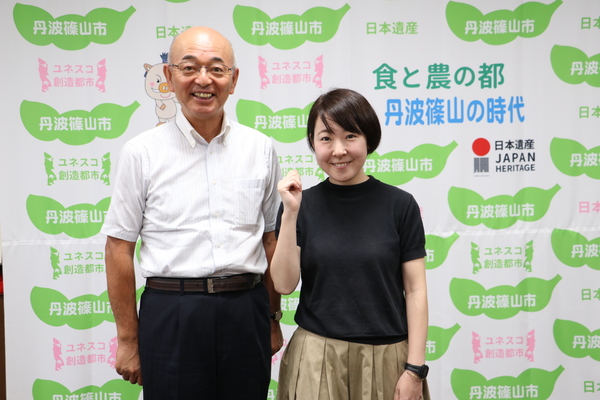 丹波篠山市と書かれた壁の前で市長と仲田さんが笑顔で立っている写真