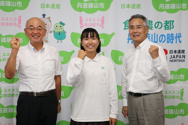 丹波篠山市と書かれた壁の前で、制服を着た金井さんと、市長、教育長がガッツポーズをして笑顔で並んでいる写真