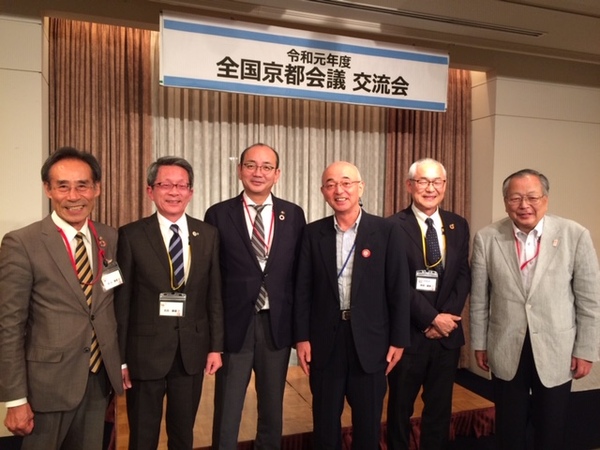 舞台の前で中央に南砺市の田中市長、丹波篠山市長、男性四名が並んで立っている写真
