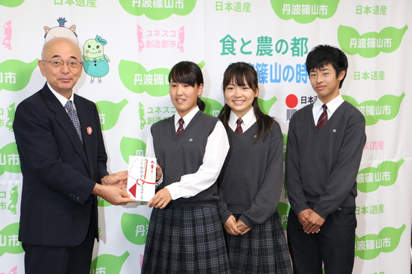 丹波篠山市と書かれた壁の前で、市長と制服を着た前川さん、藤田さん、清水くんが笑顔で立っている写真