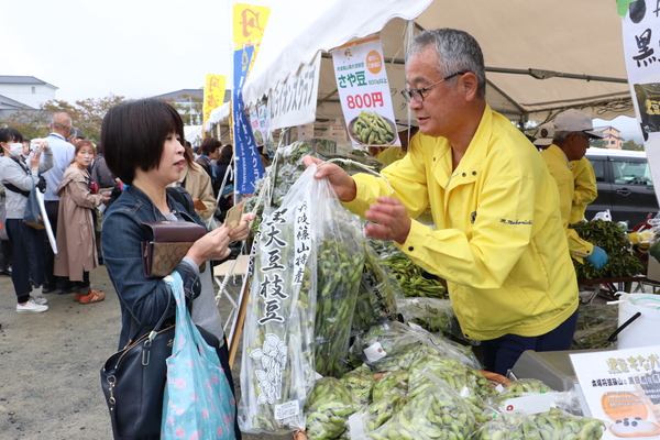 黒枝豆を購入する女性客と手渡す黄色いジャンパーの男性
