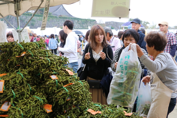 テント内に山積みになった旬の黒枝豆を談笑しながら購入する女性客の様子の写真