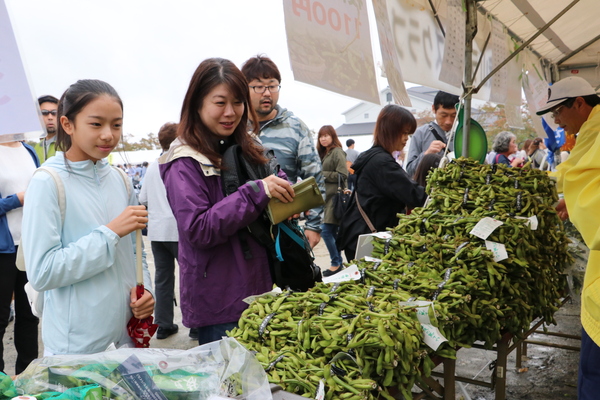 山積みの黒枝豆を前に笑顔で見つめる親子客