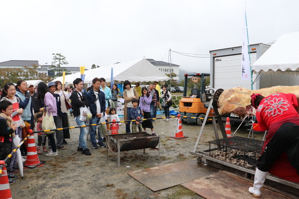 牛がセットされた大型機械をさばく男性とその周りを見つめるギャラリーの写真