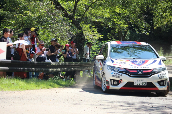 走る車を数人の観客が写真を撮ている様子
