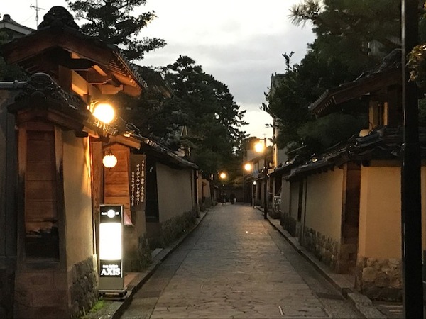 風情ある建物から植物と明かりがもれて路地がうっすらと照らされている夕暮れの様子