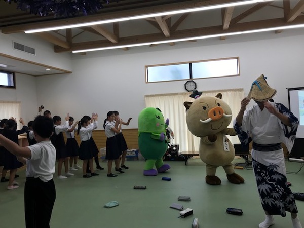 篠浴衣を着た男性職員とまるいの、まめりんのデカンショ踊りをまねて小学生たちが踊っている写真