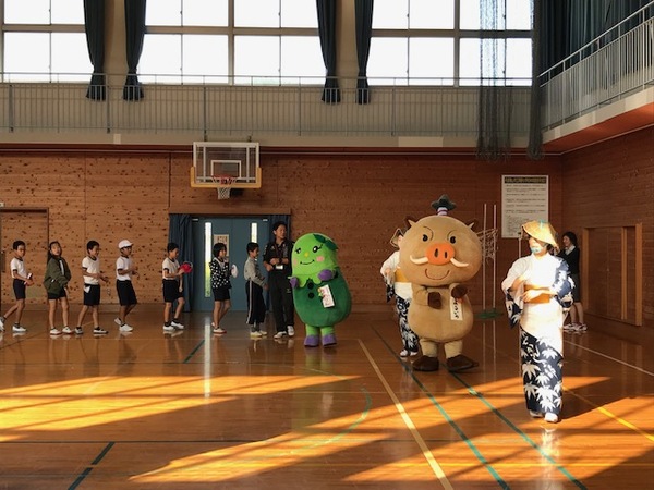 体育館で篠浴衣を着た職員を先頭に、まるいの、まめりんを真似て踊りながら列をつくる小学生たちの写真