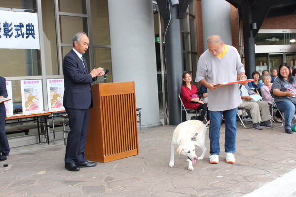長寿犬が飼い主と一緒に表彰状を受け取っている写真