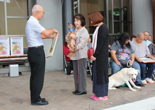 長寿犬が飼い主に抱かれて市長から表彰状を受け取っている写真
