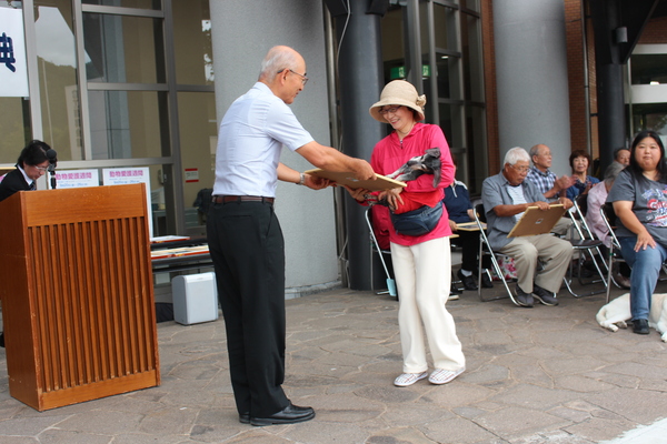 長寿犬が飼い主に抱かれながら市長より表彰状を受け取っている写真