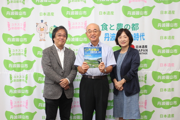 丹波篠山市と書かれた壁の前で内山さん、市長、松田さんがくるり丹波篠山の本をもって立っている写真