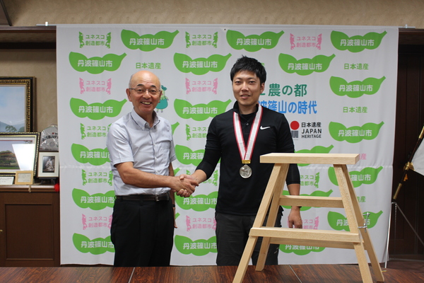 丹波篠山市と書かれた壁の前で市長とメダルを首にかけた園田さんが笑顔で握手している写真
