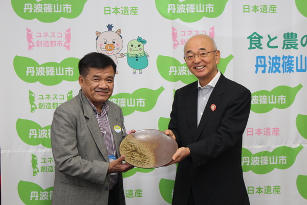 丹波篠山市と書かれた壁の前で市長とチェンマイの方が丹波焼のお皿を一緒にもっている写真