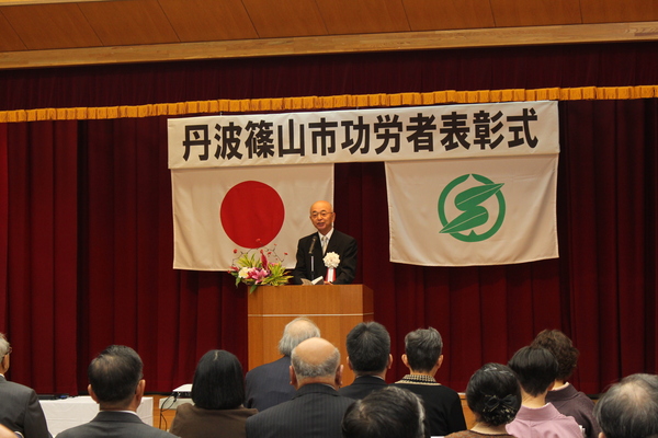 丹波篠山市功労者表彰式典舞台上に市長がマイクの前で話されている様子の写真