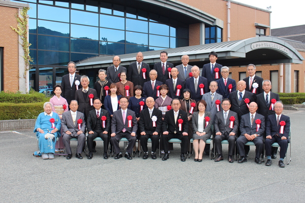 市長を囲み功労者表彰された方々が胸元に赤い花を着け整列している写真